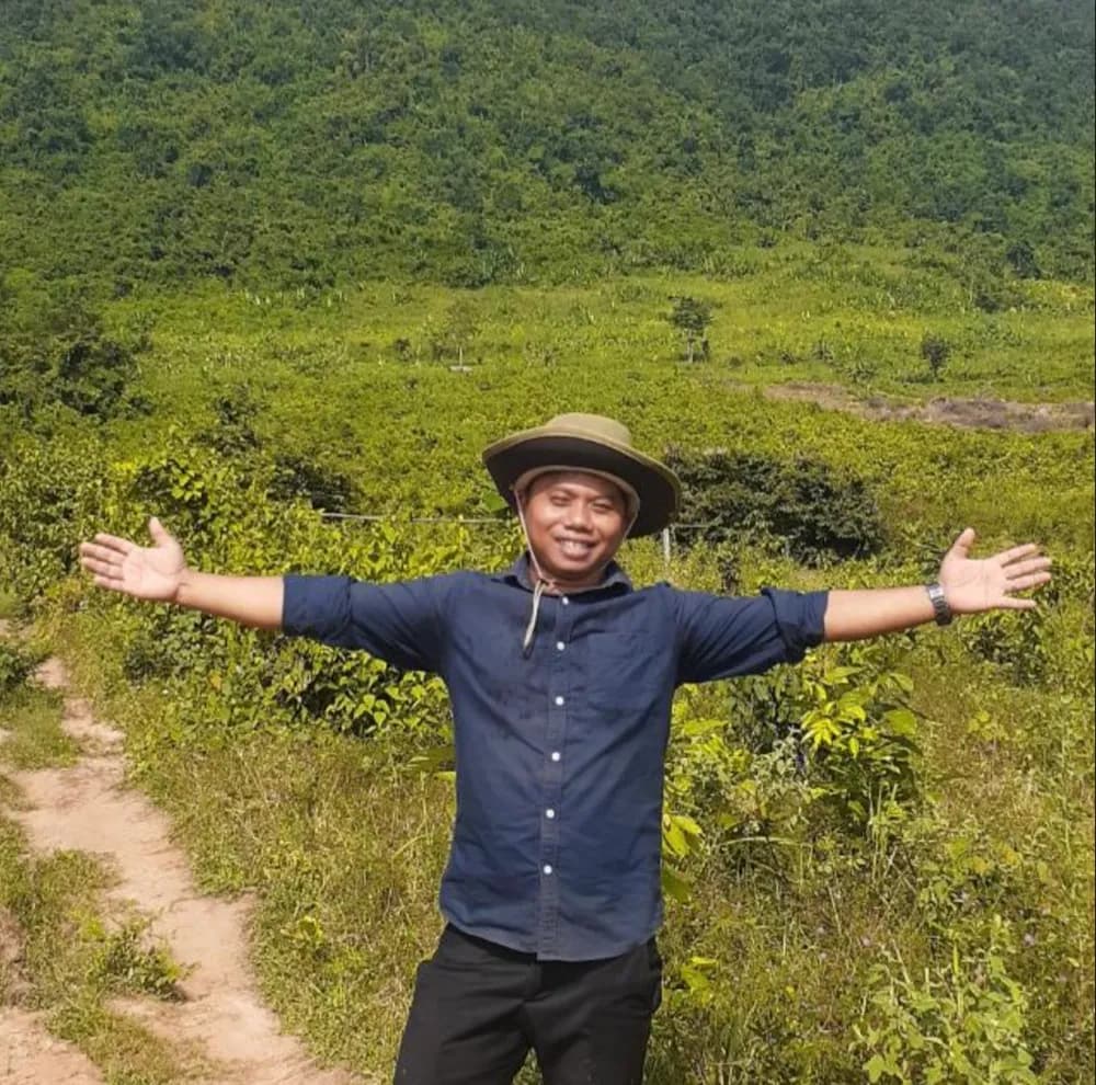 Pheakdey Chhem standing in a green field near Kampot, arms wide open, smiling under a wide-brim hat